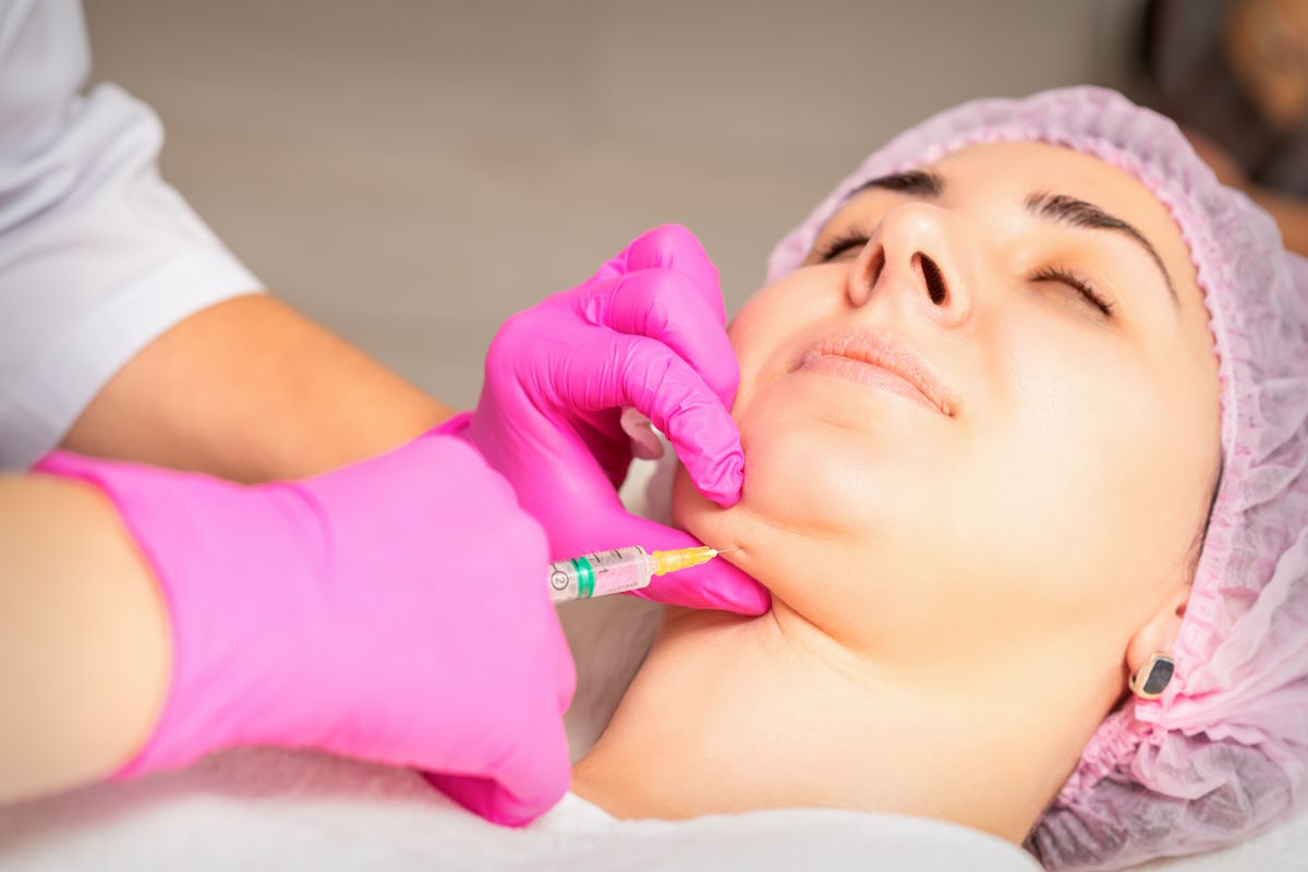 The cosmetologist makes lipolytic injection on the chin of a young woman against the double chin in a beauty salon